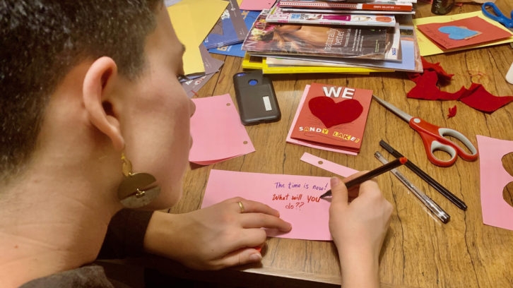 A woman writes a message on a piece of paper that says "the time is now! What will you do?"