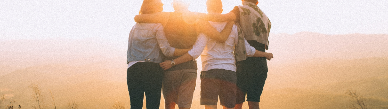 four people stand facing away from the camera with their arms around each other