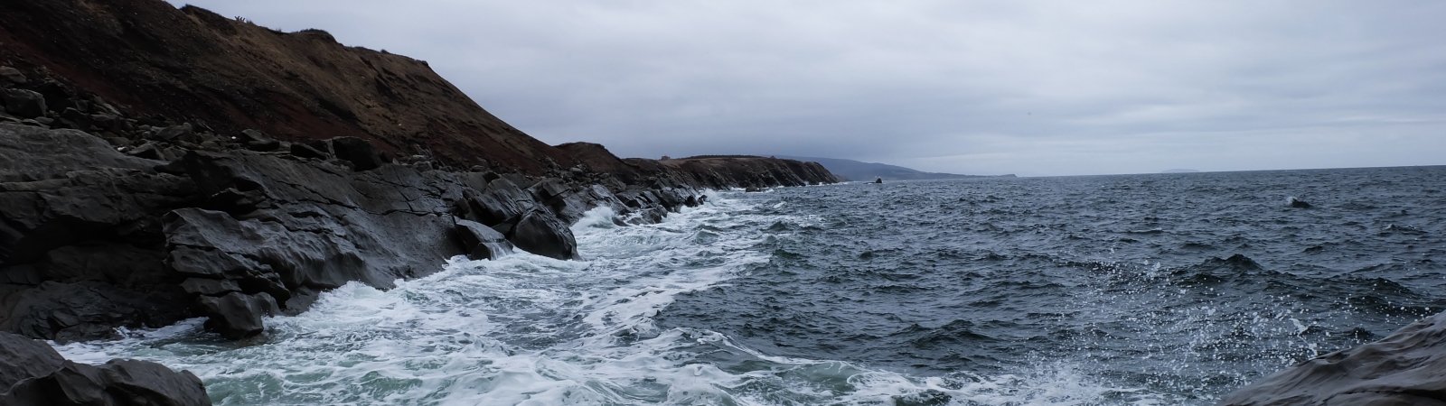 waves crash against rocks under a cloudy sky during the daytime