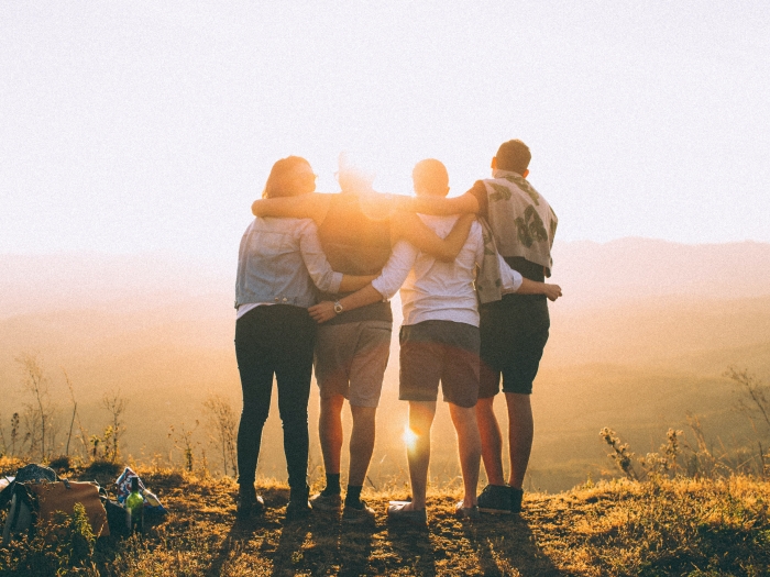 four people stand facing away from the camera with their arms around each other